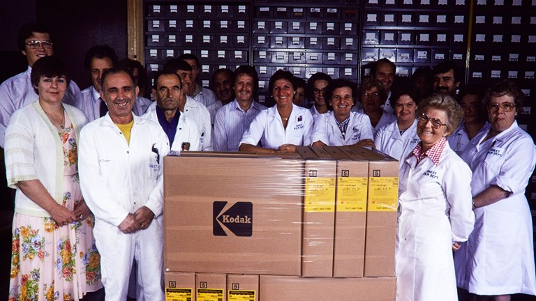 Group of staff in white lab coats standing with boxes on a pallet