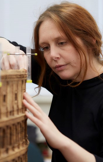 An auburn-haired woman works on a cork model of a Roman Colosseum