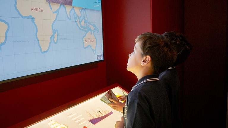 A boy looking up at the screen with a lit up world map showing Africa and Australia.