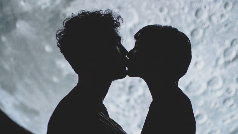 A silhouette of two people kissing in front of a projection of the moon surface