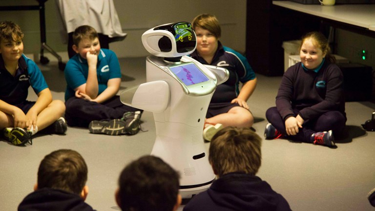Group of school children sitting in a circle around a robot