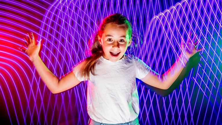 Girl standing with her arms out stretched in front of a wavy purple light