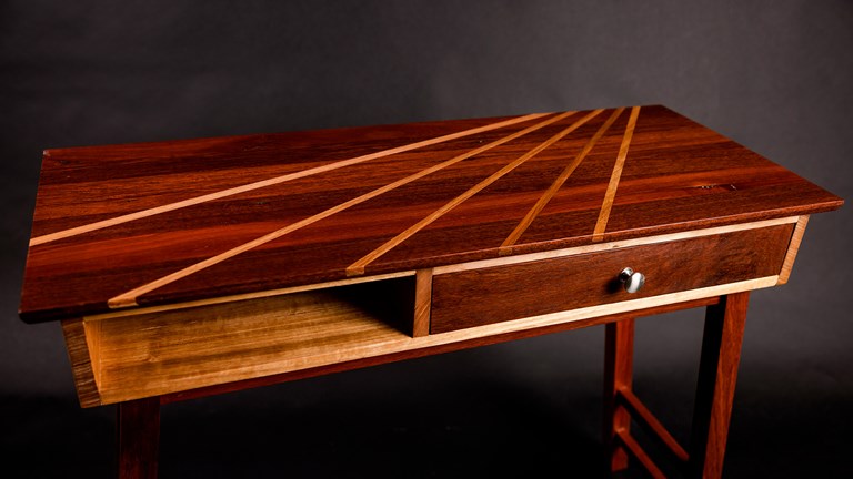 Wooden table with a drawer on the right. A sunray pattern is inlayed on the top