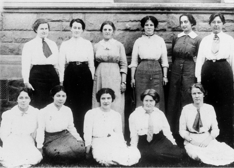 a black and white photo of 11 young women pose in front of a brick wall for a photograph 