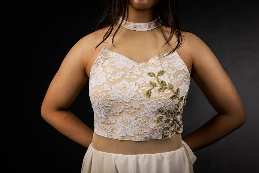 A close-up photo showing the front of a garment with a lace bodice and neckline, connected with skin-coloured panels. The top of a white skirt is visible in the photo.