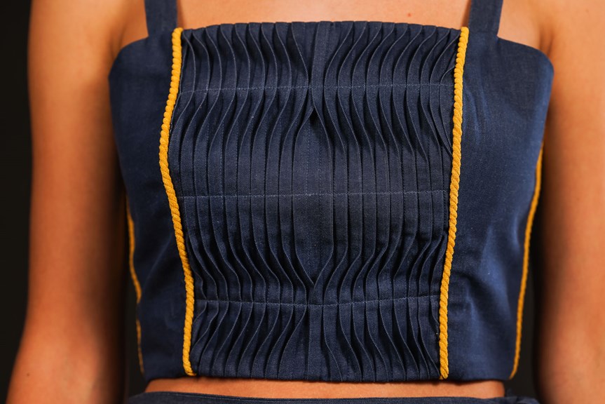 A close-up photo of a person wearing a denim bodice. The image captures the details of the bodice’s construction, showing pleating and yellow braided trim.