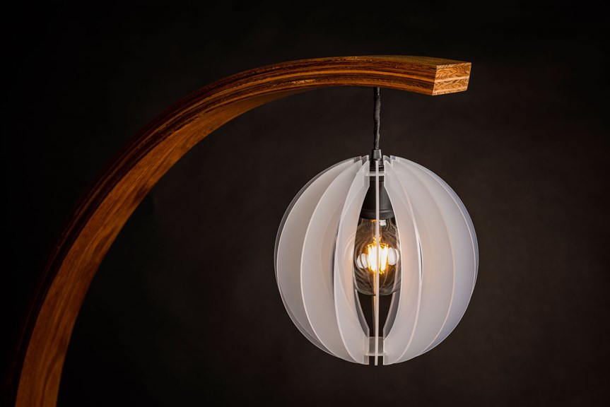 This photo is a detail from the top of the lamp/planter. A spherical lampshade made from intersecting pieces of white acrylic hangs on a black cord from a curved piece of reddish timber. The lightbulb is visible through the lampshade.