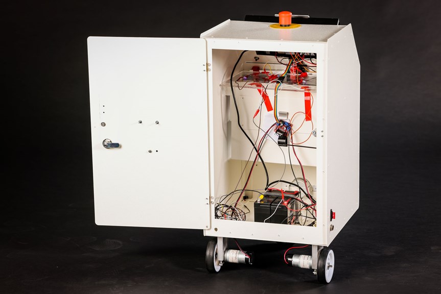 A white system on wheels is pictured with its door open. Inside the system, various wires and electronic components are visible. There is a large orange button on top of the system. 