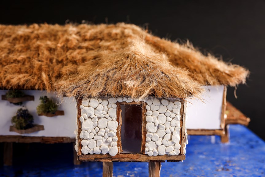A close up of an architectural model, showing a doorway surrounded by white pebbles and a thatched roof.