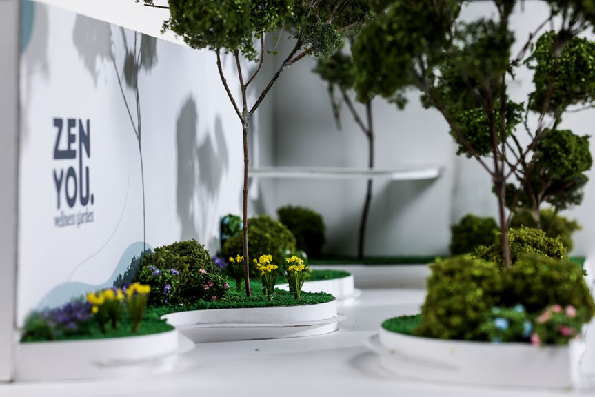 A close-up image of an architectural model. There is a curved path intersecting garden beds. An interior wall on the model has text reading ‘ZenYou Wellness Garden’.