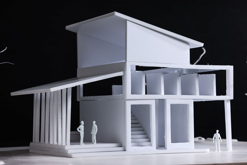 An architectural model of a white building with three levels. It is angular, with open spaces. Three model people stand around its base.