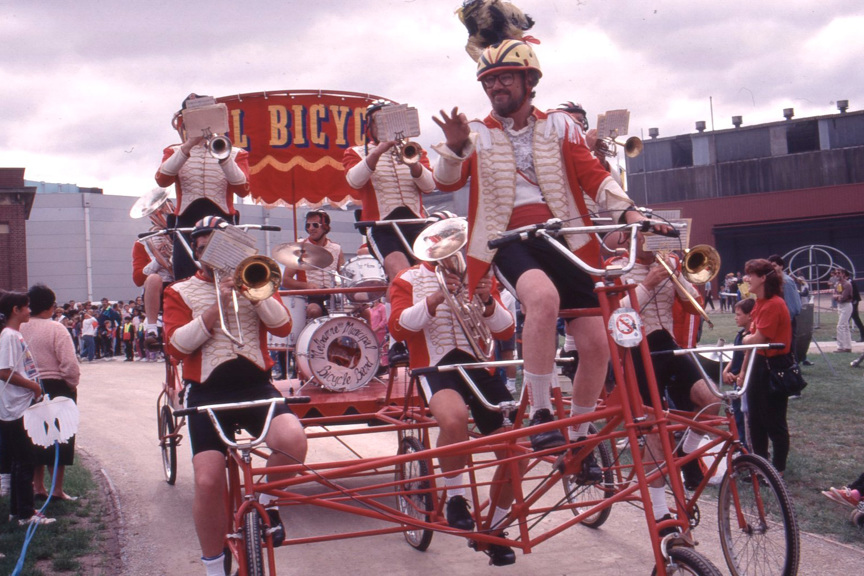 A band riding a large tricycle playing musically instruments
