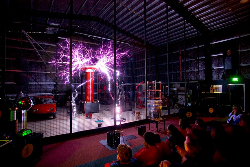 a dark room with a tall red cylinder arcing out purple bolts of electricity