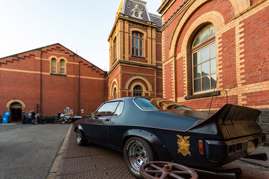a low-slung black car in front of a large brick building