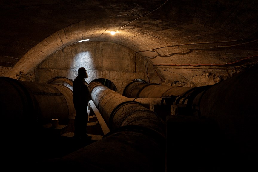 a photograph of a man silhouetted in a tunnel with three large pipes 