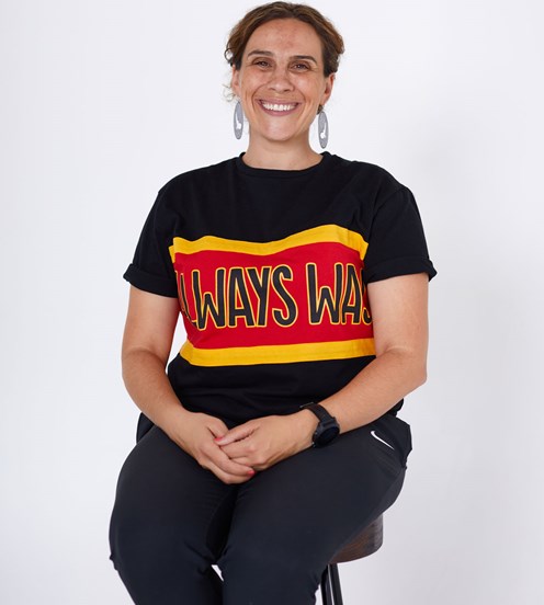 Portrait of woman sitting on a stool. She is wearing a black t-shirt printed in red and yellow