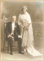 Woman in dress with train standing next to a seated man in suit.