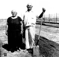 Two people standing in field, one holding a shovel.