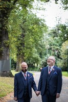 Two men in suits holding hands in park