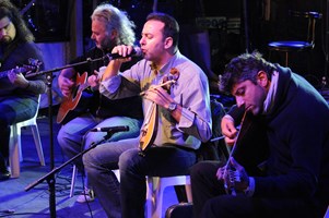 Three guitarists and a singer seated and playing music