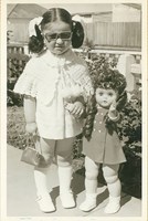 Young girl in sunglasses standing next to a doll