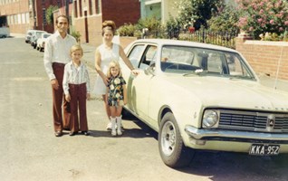 Family standing proudly next to a 1970s car