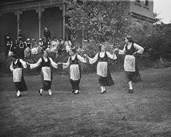 Five women perform Greek dancing on a lawn.