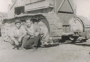 Two men crouch in front of a large bulldozer