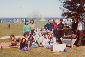 17 people of various ages, standing and sitting on picnic blankets.