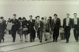 10 people walking towards camera carrying suitcases.