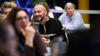 Smiling seated man with glasses in the centre, men and women seated in the background