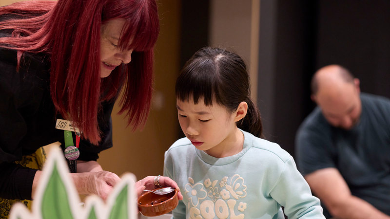 A programs officer helps a small child learn about potting seeds during Seed Stories workshop at Melbourne Museum.