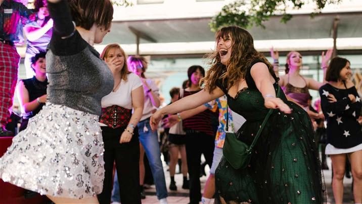A crowd of young people dancing and laughing at Immigration Museum during night at the Musuem.