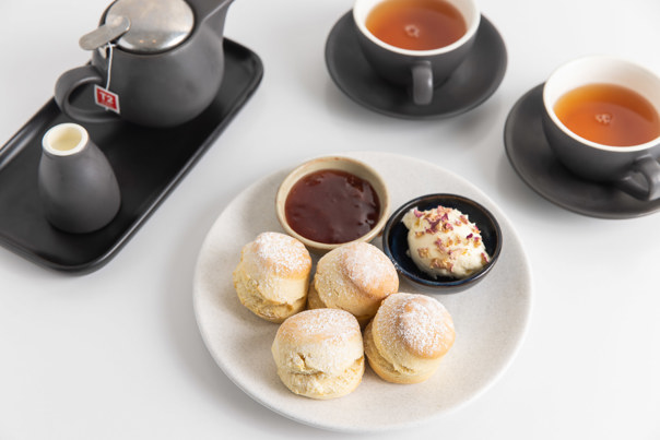 Two cups of tea served with freshly made scones, forest berry preserve jam and clotted cream.