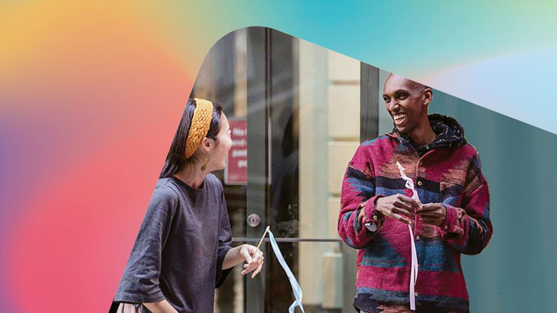 Two people laughing together while holding streamers on sticks.