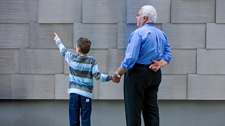 A young and an older visitor view the memorial wall in the Tribute Garden at Immigration Museum.