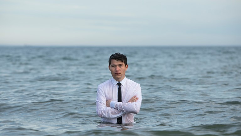 One man standing in the middle of the blue ocean with arms crossed