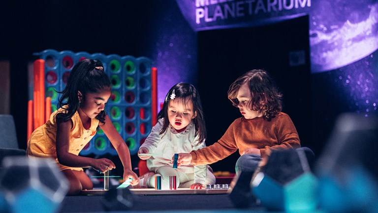 Three young children play with a light table in the Tiny Tinkerers space at Scienceworks on Little Kids' Day In