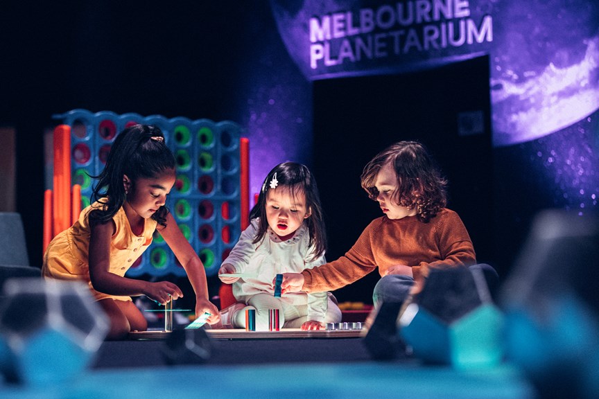 Three young children play with a light table in the Tiny Tinkerers space at Scienceworks on Little Kids' Day In