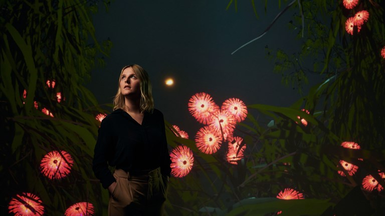 A woman surrounded by digital imagery suggesting a jungle with luminous blossoms