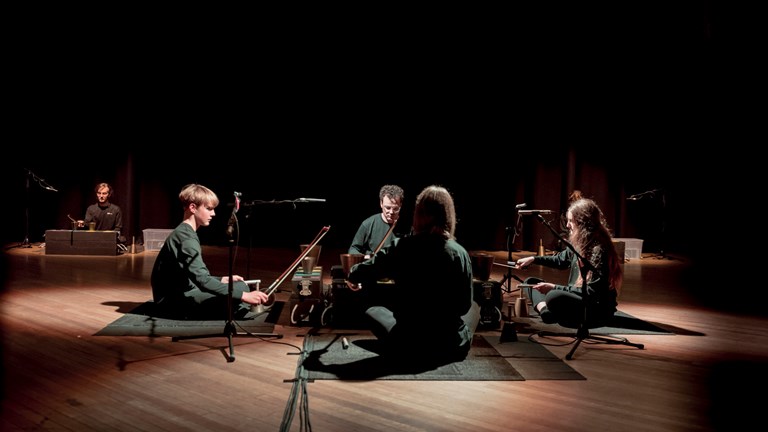 Five musicians seated on the floor, performing