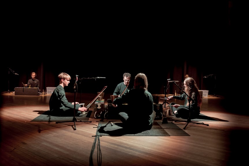 Five musicians seated on the floor, performing