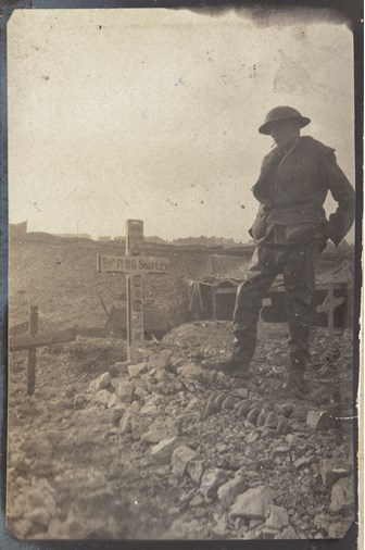 a black and white photo of a soldier standing next to a grave marked with a cross