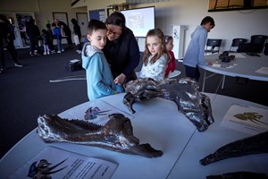 Adults and children touching large dinosaur bones on a table