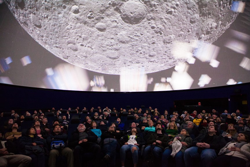 Audience members at the Planetarium are seated and looking up at the full dome