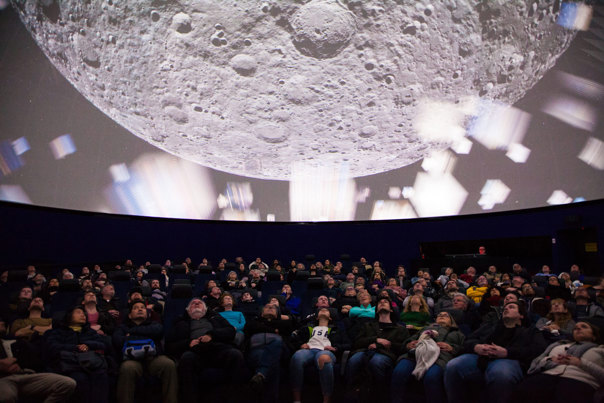 Audience members at the Planetarium are seated and looking up at the full dome