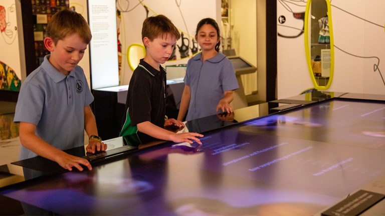 A young girl and two young boys playing with interactive exhibit.
