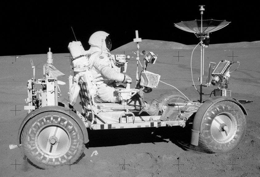 a black and white image of an astronaut driving a small buggy 