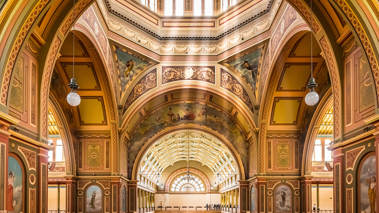 Interior of the Royal Exhibition building showcasing intricate wood paneling painted with allegorical scenes.