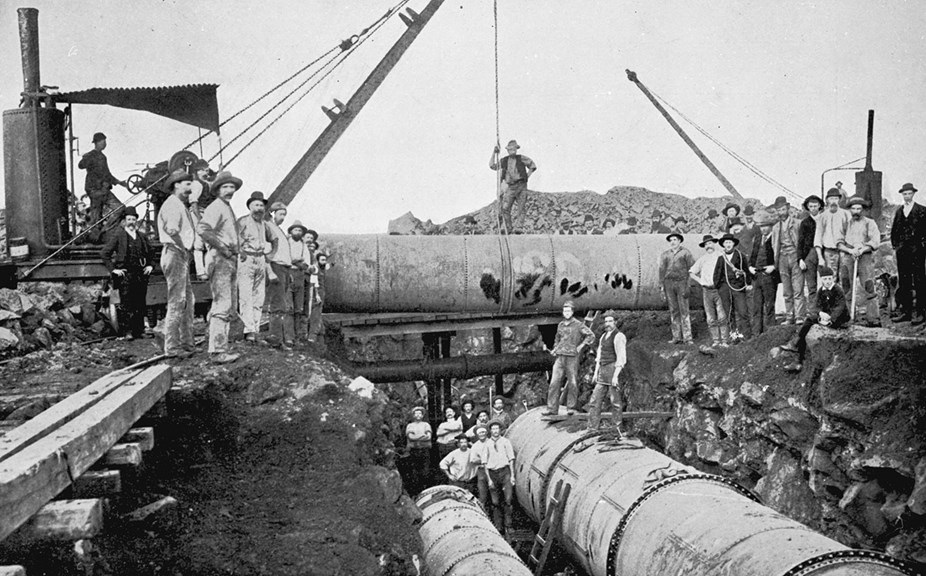 a black and white photo of a group of men standing on large pipes